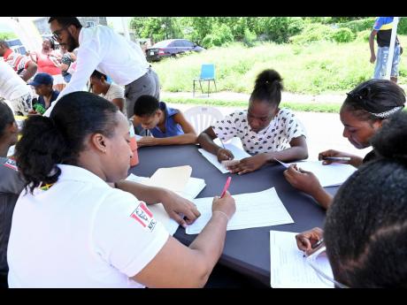 Credit: Rudolph Brown Kamilah Morrison Tucker (left) recruitment coordinator of Restaurants of Jamaica, assists members of the community to sign up for jobs within the organisation’s various franchises.