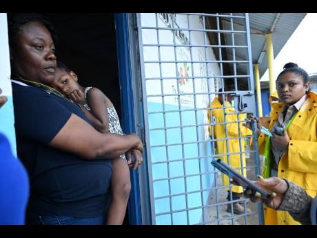 Simone Nelson (left) holds her three-year-old daughter while speaking with public health officials at the Papine High School, which is being used as a shelter.
