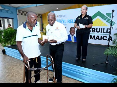Credit: Rudolph Brown Minister of Labour and Social Security Pearnel Charles Jr (centre) presents Sessil Brown with his cheque under the Rebuild Jamaica Initiative. Looking on is Colette Roberts Risden, permanent secretary in the ministry.