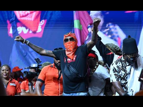 Vybz Kartel (centre) raises his clenched fists in a show of support for the People’s National Party at its annual conference held at the National Arena yesterday.