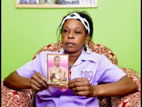 A mourning Stacy-Ann Dunkley wears the uniform shirt of her son Raniel Plummer, while displaying his photo.