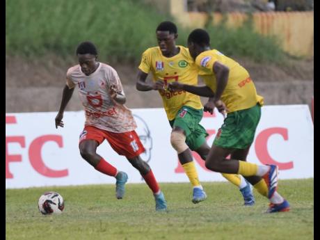 Javier Dunn (left) of Mona High School dribbles away from Jordon Taylor (centre) and Tahir Beckford of St. Jago High School during their ISSA Manning Cup football match at Stadium East on Friday.