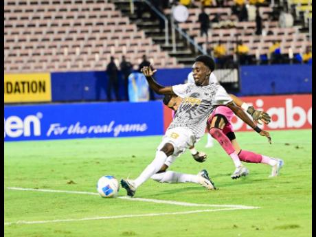 Shaquille Stein (foreground) of Cavalier Soccer Club rounds goalkeeper Miguel Baez of Moca FC to apply the finishing touch for his second goal, in time added in the first half, during the Concacaf Caribbean Club championship semifinal football fixture at the National Stadium in Kingston last night. Cavalier won 7-0. 