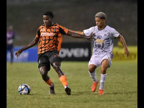 Credit: Ian Allen Denville Watson (left) of Tivoli Gardens Football Club is pressured for the ball by Kaile Auvray of Cavalier SC during their Jamaica Premier League football match at Stadium East yesterday. The game ended 1-1.