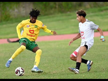 Reece Roman (left) of St. Jago High takes on Damario Brown of Mona High during the Walker Cup KO football match at Stadium East yesterday. Mona won 3-0.