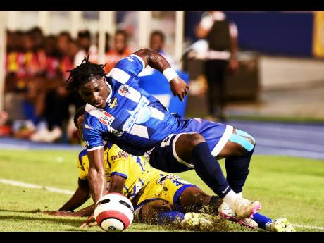 Credit: Ian Allen Alex Folkes (grounded) of Hydel High School cuts down Jamaica College’s (JC) Jamoy Dennis (right) with a tackle during their ISSA WATA Champions Cup KO football match at the National Stadium on Wednesday. JC won 1-0.