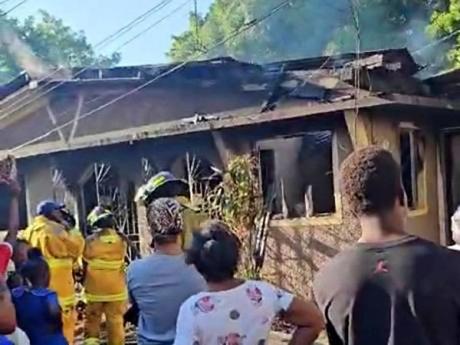 Credit: Contributed Firefighters conduct cooling-down operations while residents look on at a house fire on Whitehall Avenue in St Andrew. The fire claimed the life of a five-year-old girl.