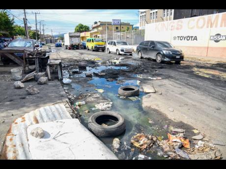 Credit: Matthew McKoy Motorists navigate the potholes and sewage along Waltham Park Road yesterday, as persons protested the state of the roadway.