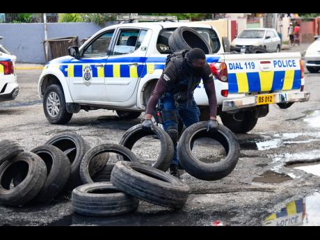 Credit: Matthew McKoy Photos A policeman removes old tyres which were among the items used to block the road.