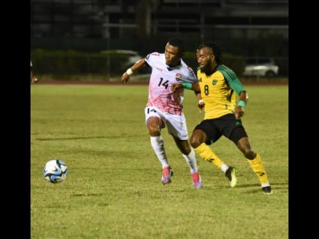 Credit: Ashley Anguin Trinidad & Tobago John-Paul Rochford (left) and Jamaica’s Demario Phillips battle for the ball during an international friendly football match at the Montego Bay Sports Complex on Thursday night. Jamaica won 1-0.