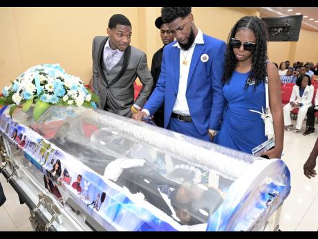 Credit: Rudolph Brown Photos Andrew ‘Bum Bam’ Cox (centre) viewing the remains of his late father, Donald ‘Danny English’ Cox, at the thanksgiving service to celebrate his life yesterday at Perry’s Hall of Thanksgiving in St Catherine. He is being consoled by his sister, Danielle Cox (right), and brother, Suen Cox.