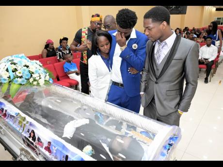 Credit: Rudolph Brown Andrew ‘Bum Bam’ Cox (centre), son of the late Donald ‘Danny English’ Cox, being comforted by Jada Jackson (left) while his brother, Seun Cox, looks on the remains of their father.