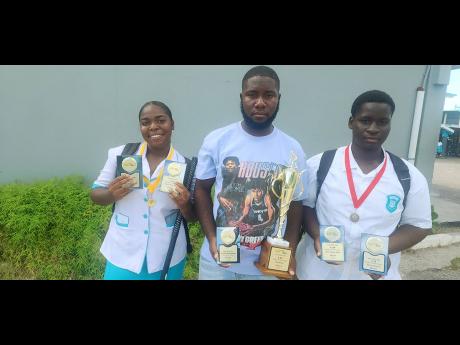 Credit: Contributed Head coach of Denbigh High School’s hockey teams, Richard Piper, displaying trophies won by his team in the ISSA boys and girls’ competitions this season. He is flanked by female MVP Nishauna Forshaw and male MVP Jason Channer.