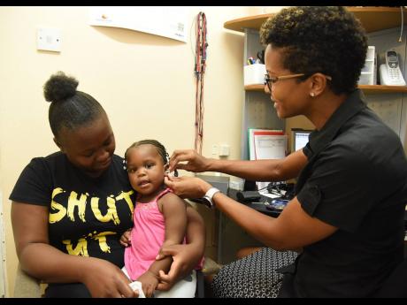 Credit: Ian Allen Photos Little Azaria Brighton (centre) gets fitted with hearing aids by Kristen Metz, senior audiologist assistant at Caribbean Hearing Centre, while her mom Anneil Richards looks on.