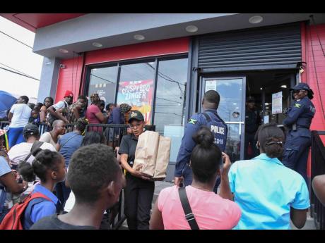 Credit: Antoine Lodge Members of the Jamaica Constabulary Force try to manage the large crowd outside the KFC Rockfort branch in Kingston yesterday.