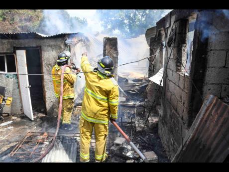 Credit: Antoine Lodge Firefighters perform cooling-down operations as a fire destroyed several homes along Price Lane in the Rose Gardens community of Kingston yesterday.