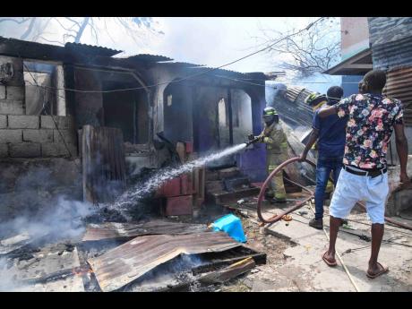 Credit: Ashanti Lawson Photo A member of the Jamaica Fire Brigade helping to quell the blaze as residents offer some assistance.