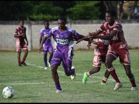 Irwin High’s Earl Anderson (left) dribbles the ball away from Herbert Morrison’s Zaahir Davis (right) during their Zone A football match in the ISSA daCosta Cup competition at Irwin High yesterday. Irwin won 3-0.
