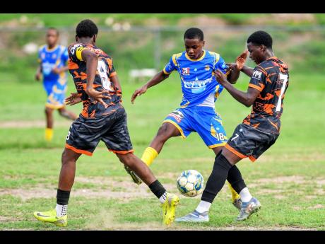 Credit: Matthew McKoy Tarese Morgan (centre) of Tarrant High School tries to manoeuvre between Malachi Rose (left) and Davonique Gouldbourne of Tivoli Gardens High during the ISSA WATA Manning Cup football match at Tarrant High School in Kingston yesterday. Tivoli Gardens High won 5-0.