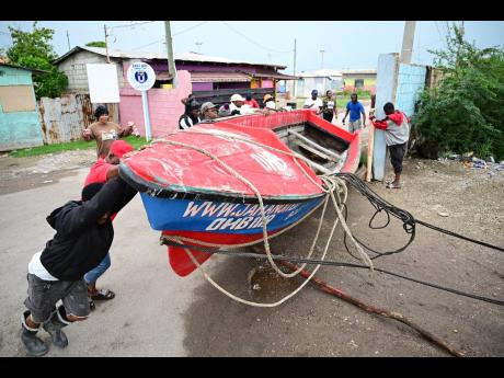 Credit: Gladstone Taylor/Multimedia Photo Editor Members of the community assist in securing this boat at the Old Harbour Bay Fishing Village yesterday.