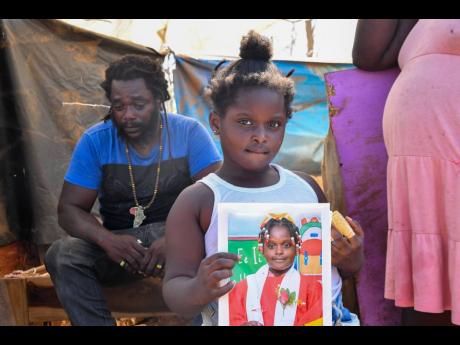 Six-year-old Jermonique Tomlinson shows off her graduation photo, one of the handful of treasures rescued from the wreckage of Hurricane Melissa.