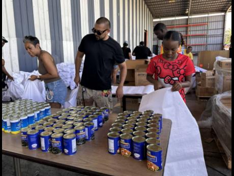 Credit: Contributed International recording artiste Sean Paul (centre), his sister-in-law Winsome Henriques (left), and a volunteer of the Sean Paul Foundation, Alana Thomas, get ready to package food items during their visit to the Food For The Poor Jamaica.
