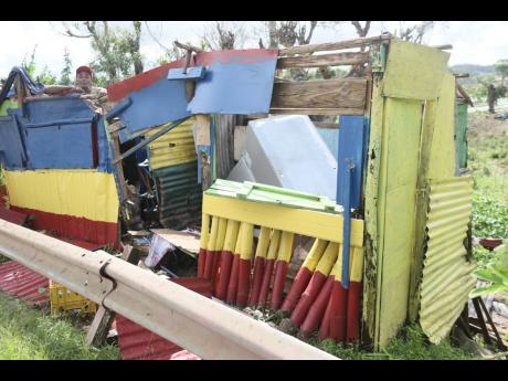 Credit: Nathaniel Stewart Burnell Morris of Cobbla, Manchester uses a tarpaulin to cover his shop along the main road after the structure was damaged during the passage of Hurricane Melissa.