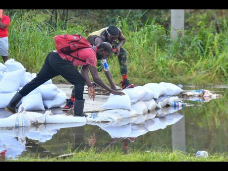 Credit: Matthew McKoy Residents using sand bags to prevent the water from rising any further along the main road in Content.