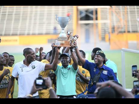 Coach of Clarendon College, Devon Anderson (centre), holds aloft the Ben Francis Cup football trophy after his team defeated Cornwall College 2-1 at the National Stadium on December 20, 2025.