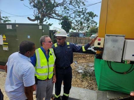 Credit: Contributed JPS President & CEO Hugh Grant (right) explains the operation of the new JPS Emergency Mobile Power Generation Unit to Minister of Energy Daryl Vaz (centre) and Floyd Green, member of parliament for St Elizabeth South Western. The mobile unit will power several communities including Treasure Beach and Calabash Bay.