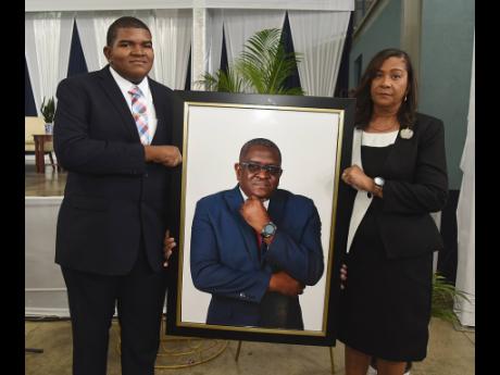 Karen Smith (right), the widow of Anthony Smith, and her son Daniel Smith (left), hold a picture of the late CEO of the RJRGLEANER Communications Group, during a thanksgiving service for his life on Sunday at the Karl Hendrickson Auditorium at Jamaica College.