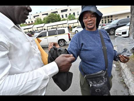 A customer collects his bag from Simone ‘Shelly’ Henry, who keeps phones and bags safe outside the US Embassy in Kingston.