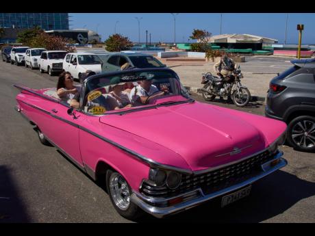 Tourists travel in a classic American car next to a line of drivers waiting to buy fuel for their cars in Havana, Cuba, yesterday.