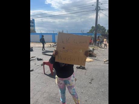 A resident of Jones Town bears a placard calling for justice for former footballer Lucien Anderson who was killed in an alleged confrontation with police on Sunday. The protest was on Slipe Pen Road in Kingston yesterday.