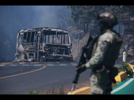 A soldier stands guard by a charred vehicle after it was set on fire, in Cointzio, Michoacán state, Mexico, on Sunday, February 22, following the death of the leader of the Jalisco New Generation Cartel, Nemesio Oseguera, known as “El Mencho”.