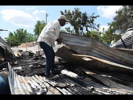 Clive Evans shifts sheets of zinc in hope of salvaging something after fire destroyed his four-bedroom house.