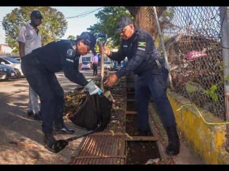 Police Inspectors Heather Mclean (left) and Hugh Lewis of the Constant Spring Police Station, clear leaves and other debris from a drain at the Constant Spring Police Station during a clean-up activity at the station grounds in St. Andrew on Saturday (February 21). The exercise involved partnership with the National Solid Waste Management Authority (NSWMA). 

